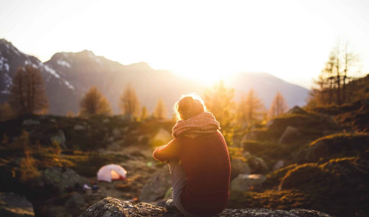 Woman sitting on a rock watching the sunset over a mountain range in a forest
