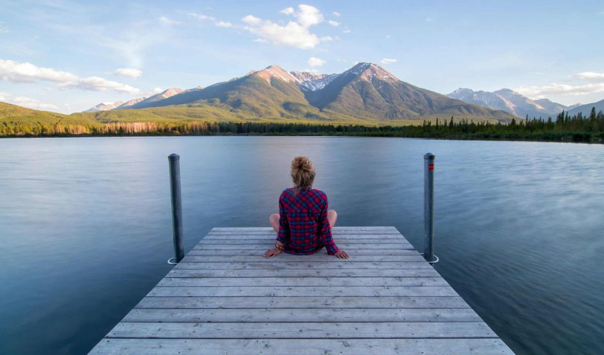 Woman sitting on a lake dock overlooking a mountain range