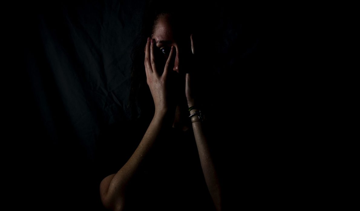 Young girl holding her hands over her face in a dimly lit room