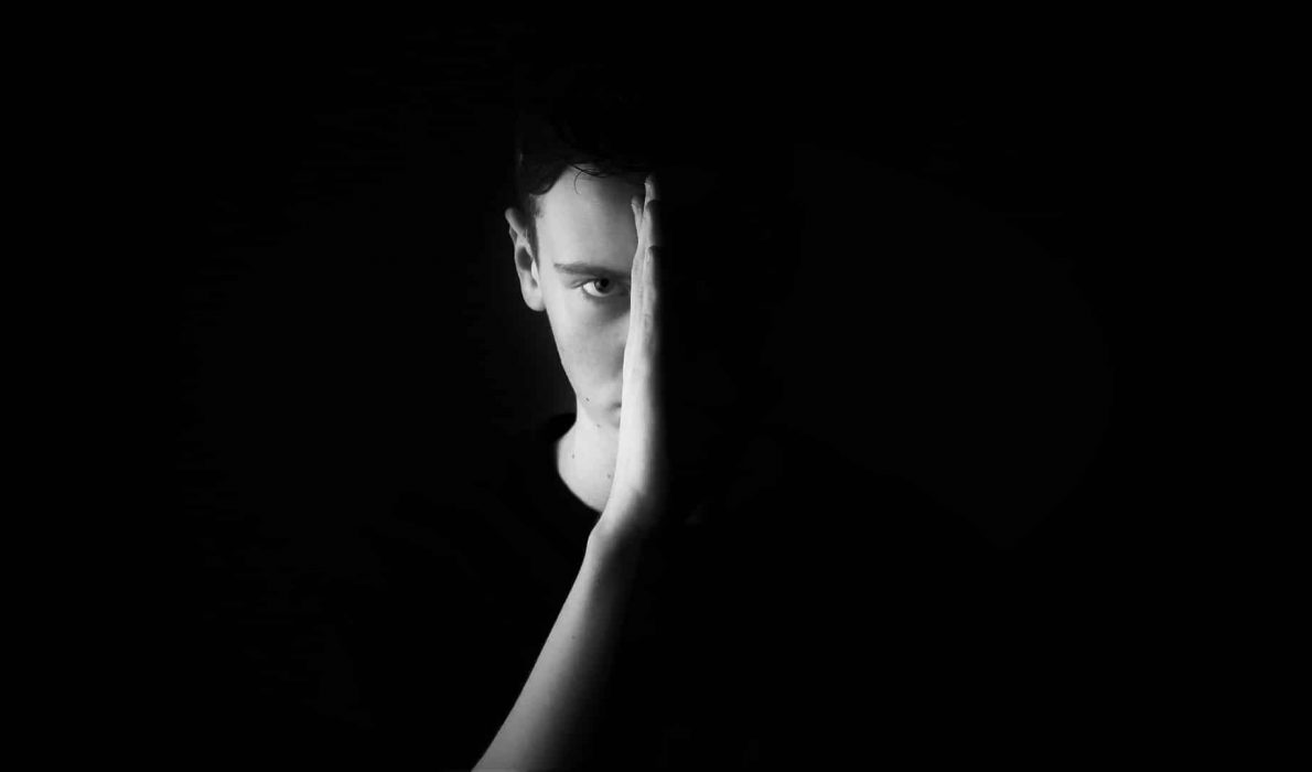 Young man holding his hand in front of his face with one eye showing