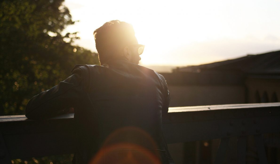 Man looking over deck railing with a sunrise in the distance